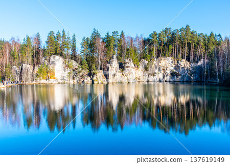 Piskovna Lake in Adrspach Rocks showcases stunning natural beauty. Surrounded by tall trees and rock formations, the calm water reflects the serene landscape on a clear day. Piskovna Lake in Adrspach Rocks showcases stunning natural beauty. Surrounded by tall trees and rock formations, the calm water reflects the serene landscape on a clear day. 137619149