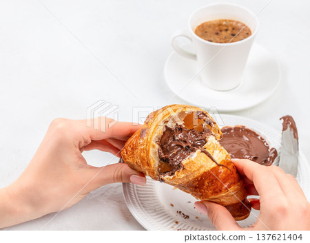 Woman breaking chocolate croissant with coffee breakfast scene Woman breaking chocolate croissant with coffee breakfast scene 137621404
