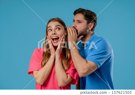 Gossiper man whispers in womans ear secret, rumors, gossips, blue studio. Pretty lady and handsome guy - couple, shh, conspiracy concept Gossiper man whispers in womans ear secret, rumors, gossips, blue studio. Pretty lady and handsome guy - couple, shh, conspiracy concept 137621505