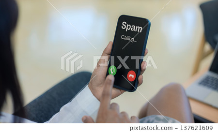 Spam call notification on smartphone screen alert. Cyber scam and telemarketing fraud protection concept. Mobile security and identification. Woman holding phone with unwanted spam call display. 137621609