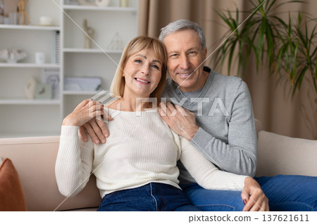 Mature couple posing together on couch at home, smiling at camera 137621611