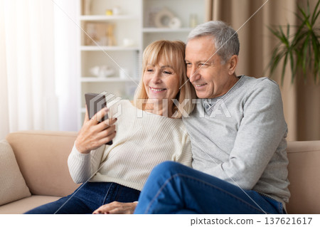 Senior couple sitting on sofa taking selfie with smartphone Senior couple sitting on sofa taking selfie with smartphone 137621617