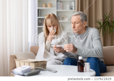 Senior couple at home checking thermometer while woman is sick and coughing 137621629
