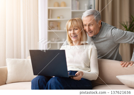 Senior couple smiling while using laptop together at home Senior couple smiling while using laptop together at home 137621636