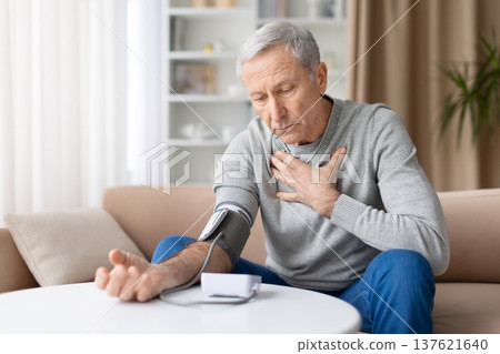 Senior man measuring blood pressure at home while experiencing chest pain Senior man measuring blood pressure at home while experiencing chest pain 137621640