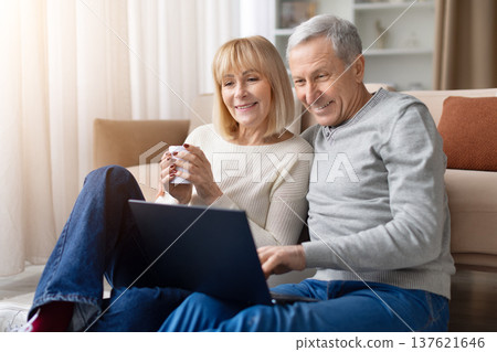 Senior couple relaxing on sofa using laptop and drinking coffee at home Senior couple relaxing on sofa using laptop and drinking coffee at home 137621646