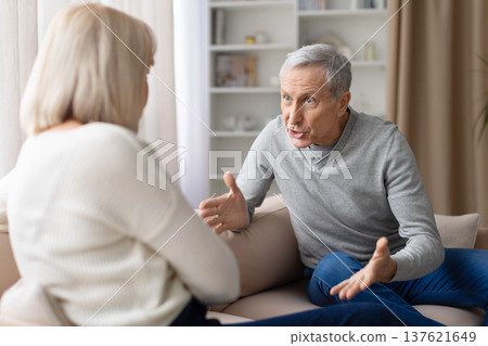 Senior couple having an emotional discussion while sitting on sofa at home Senior couple having an emotional discussion while sitting on sofa at home 137621649