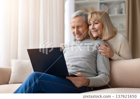 Senior couple relaxing together on sofa using laptop in bright living room Senior couple relaxing together on sofa using laptop in bright living room 137621650