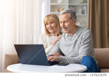 Senior couple using laptop together while sitting on sofa at home Senior couple using laptop together while sitting on sofa at home 137621670