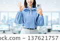 A young woman/businesswoman holding a smartphone and making an OK pose A young woman/businesswoman holding a smartphone and making an OK pose 137621757