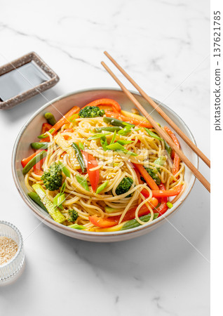 Vegetarian wok noodles with vegetables in a plate on a light marble background with chopsticks 137621785