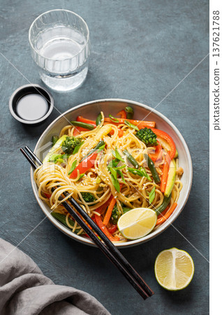 Vegetarian wok noodles with vegetables in a plate on a dark background with chopsticks Vegetarian wok noodles with vegetables in a plate on a dark background with chopsticks 137621788