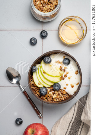 Natural greek yogurt with granola, blueberry and apple in a bowl on a blue tile background Natural greek yogurt with granola, blueberry and apple in a bowl on a blue tile background 137621802