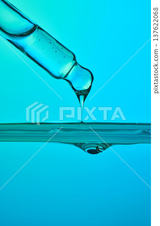 Pipette dropping blue liquid into water surface impacting 137622068