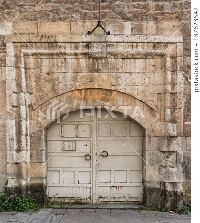Weathered stone archway and rustic white wooden door with metal ring handles on an old building facade 137623542