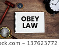Obey Law message written on notepad with alarm clock, wood gavel and magnifying glass flat lay on wooden background 137623772