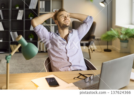 Relaxed businessman smiling after achievement at desk with laptop in office 137624366