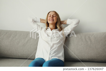Happy relaxed young woman enjoying at home, satisfied girl sitting on the couch in living room Happy relaxed young woman enjoying at home, satisfied girl sitting on the couch in living room 137626047