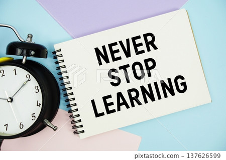 Never Stop Learning text written on notepad with alarm clock flat lay on multicolor pastel background 137626599