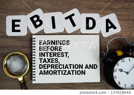 EBITDA Earnings Before Interest, Taxes, Depreciation And Amortization text on notepad with magnifying glass and alarm clock on wooden background. 137626648