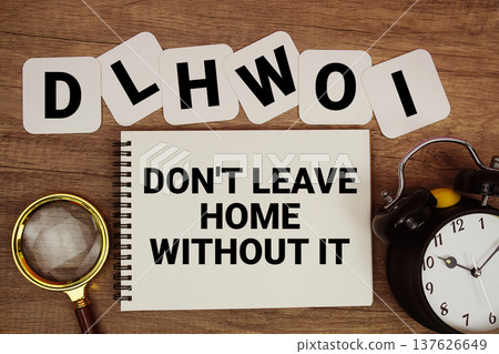 DLHWOI Don't Leave Home Without It text on notepad with magnifying glass and alarm clock on wooden background DLHWOI Don't Leave Home Without It text on notepad with magnifying glass and alarm clock on wooden background 137626649