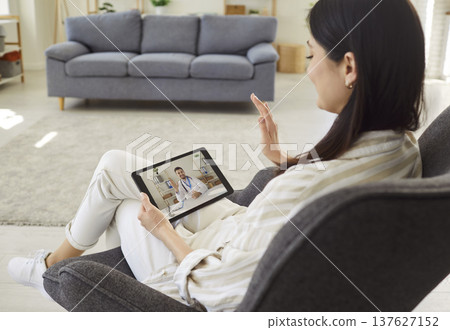 Smiling young woman discussing health issues with doctor via video call during online consultation. 137627152
