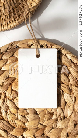 Blank White Tag Hanging on Woven Mat with Neutral Tones for Minimalist Aesthetic 137627176