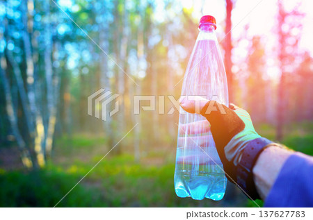 Water bottle in athlete's hand during a hike in woods. 137627783
