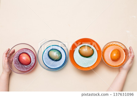 Hands of a girl child coloring festive Easter eggs with colorful dyes on the table at home 137631096