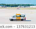 White airport transport van driving on a sunny tarmac at a busy airfield 137631213