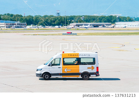 White airport transport van driving on a sunny tarmac at a busy airfield 137631213