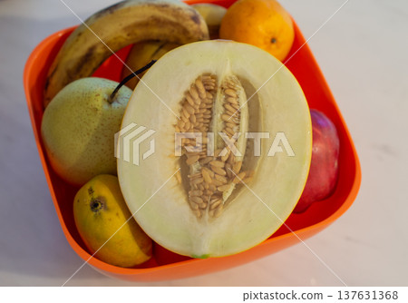 Assorted fruit in orange bowl with halved melon Assorted fruit in orange bowl with halved melon 137631368