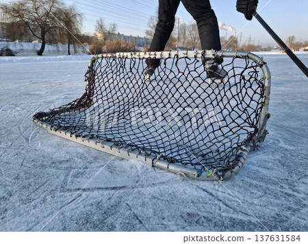 A hockey player stands on a frozen lake near a goal A hockey player stands on a frozen lake near a goal 137631584
