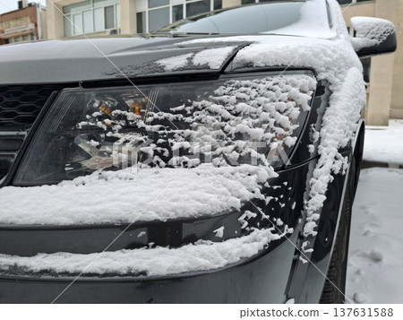 White snow lies on black car. The front bumper of a car is covered in snow White snow lies on black car. The front bumper of a car is covered in snow 137631588