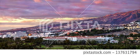 A wide panoramic view of the coastal city of Playa de las Americas at sunset with mountains in the background, Arona, Tenerife, Spain. A wide panoramic view of the coastal city of Playa de las Americas at sunset with mountains in the background, Arona, Tenerife, Spain. 137631794