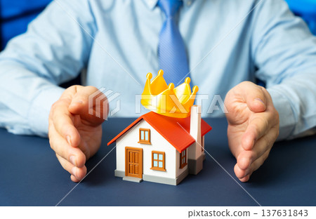 A man clasps his hands around a house with a crown on the roof. Property insurance and protection of valuable homes. Premium housing, buying and renting real estate and the idea of the perfect home. 137631843