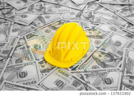 A yellow construction worker's hard hat against a background of money. Symbol of booming construction sector, real estate bubble risks and major investments in building projects, engineering A yellow construction worker's hard hat against a background of money. Symbol of booming construction sector, real estate bubble risks and major investments in building projects, engineering 137631902