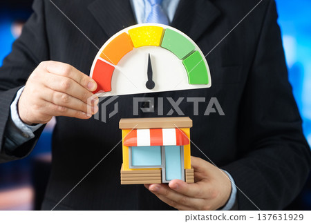 A businessman holds a store and a performance scale with an arrow pointing to the yellow level. Average business indicators and moderate sales results. Business optimization to increase profits A businessman holds a store and a performance scale with an arrow pointing to the yellow level. Average business indicators and moderate sales results. Business optimization to increase profits 137631929