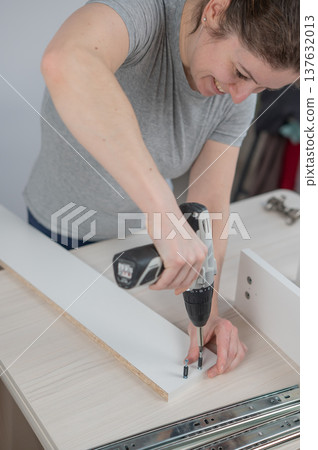A Caucasian woman uses a screwdriver to tighten a screw while assembling a cabinet. 137632013
