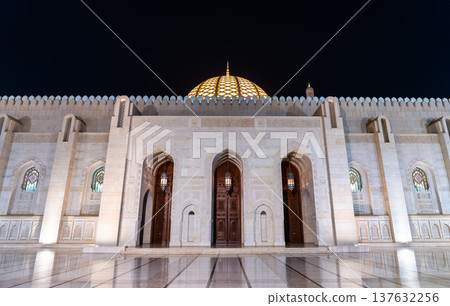 Night view of the Sultan Qaboos Grand Mosque in Muscat, Oman, featuring the illuminated dome and decorative archways of the main entrance. 137632256