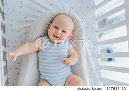 Baby lying peacefully in a cozy cocoon nest inside a crib, feeling safe and calm at home. Soft light and warm atmosphere highlight comfort and care. Infant sleep, safety and gentle parenting concept Baby lying peacefully in a cozy cocoon nest inside a crib, feeling safe and calm at home. Soft light and warm atmosphere highlight comfort and care. Infant sleep, safety and gentle parenting concept 137633483