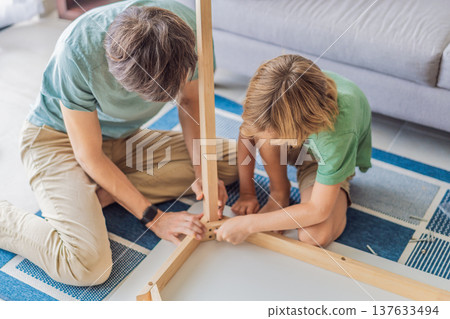 Father and his son assembling a table together in the living room at home. Meaningful family moment showing teamwork, learning and support. Fatherhood, home improvement and bonding through shared Father and his son assembling a table together in the living room at home. Meaningful family moment showing teamwork, learning and support. Fatherhood, home improvement and bonding through shared 137633494