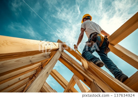 Skilled construction worker diligently installing roofing materials on a residential building under a bright blue sky. Skilled construction worker diligently installing roofing materials on a residential building under a bright blue sky. 137634924