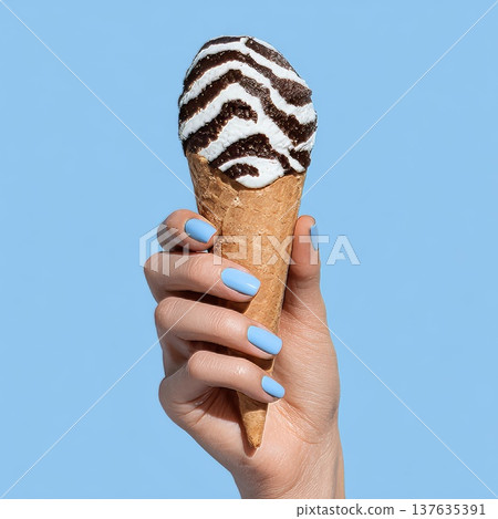 A woman's manicured hand holds an ice cream cone with white and dark stripes reminiscent of a zebra. A woman's manicured hand holds an ice cream cone with white and dark stripes reminiscent of a zebra. 137635391