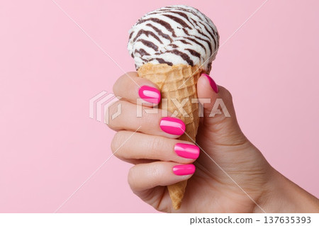 A woman's manicured hand holds an ice cream cone with white and dark stripes reminiscent of a zebra. A woman's manicured hand holds an ice cream cone with white and dark stripes reminiscent of a zebra. 137635393