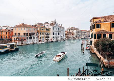 Boats travel on a canal in Venice with buildings and a cloudy sky in view Boats travel on a canal in Venice with buildings and a cloudy sky in view 137636957