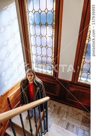Woman climbs stairs in a building with stained glass windows during daylight hours Woman climbs stairs in a building with stained glass windows during daylight hours 137636995