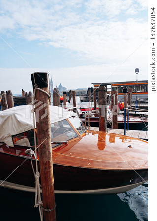 Wooden boat tied to dock at harbor near city in daytime with cloudy sky above 137637054