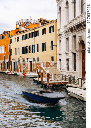 Boats move along a canal in Venice near buildings on a cloudy day Boats move along a canal in Venice near buildings on a cloudy day 137637068