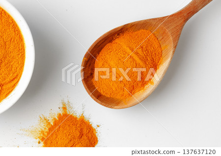 Turmeric powder in a wooden spoon and a bowl on a white surface Turmeric powder in a wooden spoon and a bowl on a white surface 137637120